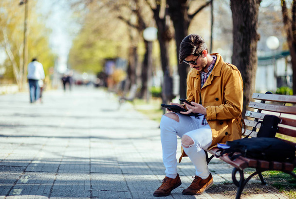Empresario urbano trabaja en la tableta mientras está sentado en el banco en el p
 - Foto, imagen