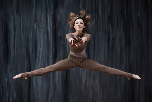 Twine in a jump. Young woman gymnast, fitness and stretching trainer shows sport exercises - 写真・画像