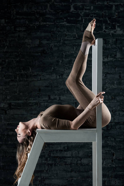 Svelte jeune femme gymnaste en combinaison posant et montrant des exercices sportifs sur un escabeau en bois
 - Photo, image