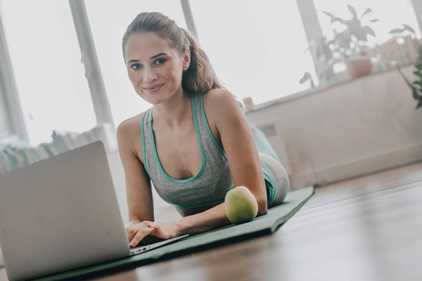 Close up of woman laying on yoga mat with laptop - Photo, Image