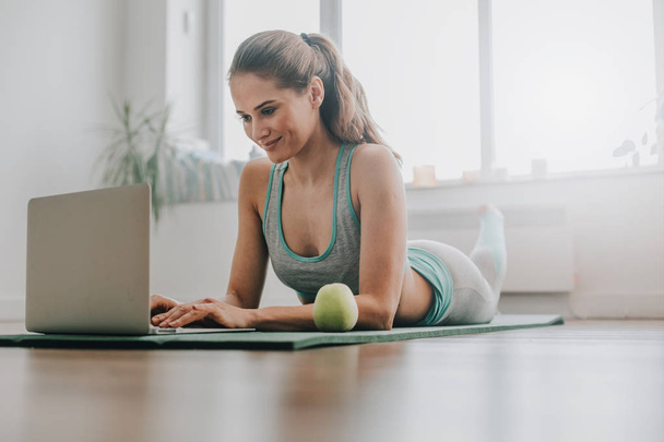 Zbliżenie kobiety układanie na matę do jogi z laptopem - Zdjęcie, obraz