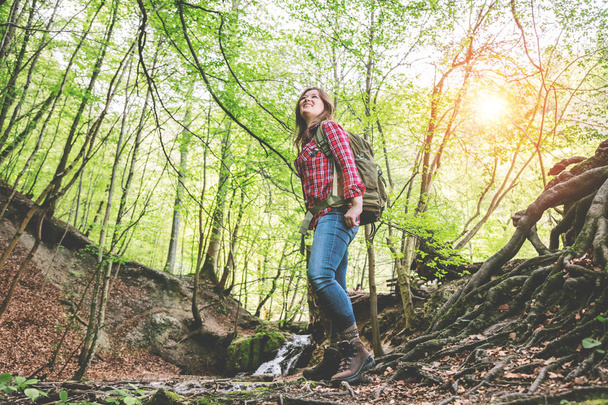 низький кут зору усміхненої молодої жінки з рюкзаком в красивому лісі
  - Фото, зображення