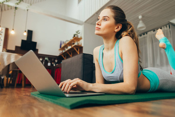 Dreamful female on yoga mat with laptop - Фото, изображение