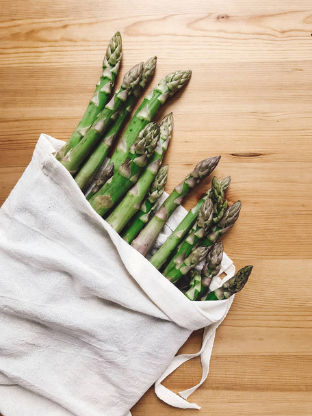 Reusable eco friendly bag with fresh asparagus on wooden table,  - Foto, afbeelding