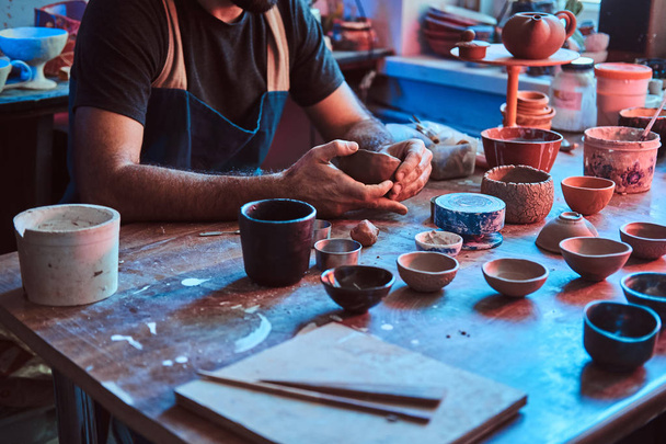 Потрясенный гончар в очках в собственной мастерской работает над новым чайником ручной работы
. - Фото, изображение