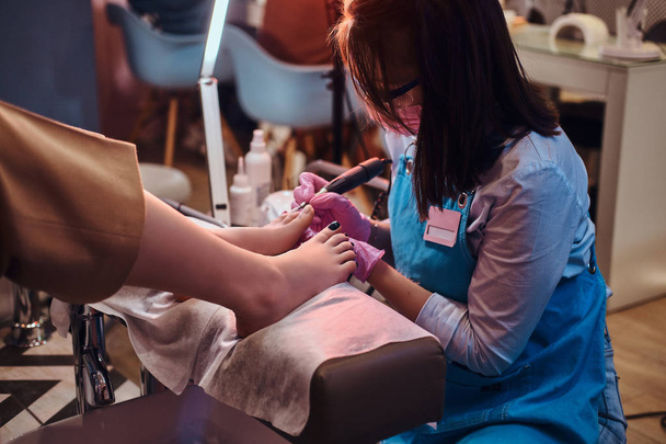 Joven maestro de uñas alegre está trabajando en los clientes uñas de los pies en su estudio de pedicura
. - Foto, imagen