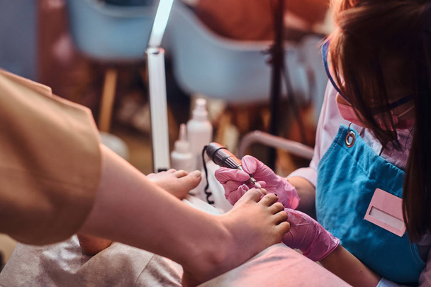Joven maestro de uñas alegre está trabajando en los clientes uñas de los pies en su estudio de pedicura
. - Foto, imagen