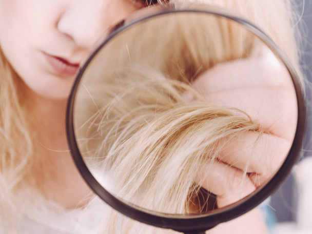 Женщина смотрит на концы волос через увеличительное стекло
 - Фото, изображение