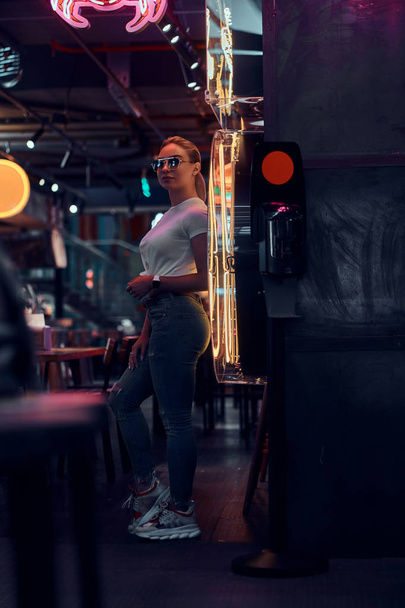 Attractive woman in sunglasses at neon bar is posing for photographer. - Φωτογραφία, εικόνα