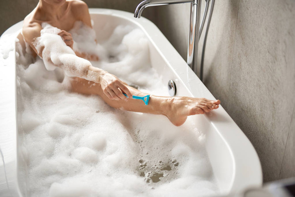 Fiatal hölgy borotválja a lábát habfürdőben. - Fotó, kép