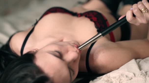 Sexy girl with black hair in beautiful red lace lingerie with a manicure with pleasure smokes a hookah on a white cotton bed in bedroom and gets enjoy at home. Woman blows smoke from her mouth. - Filmagem, Vídeo