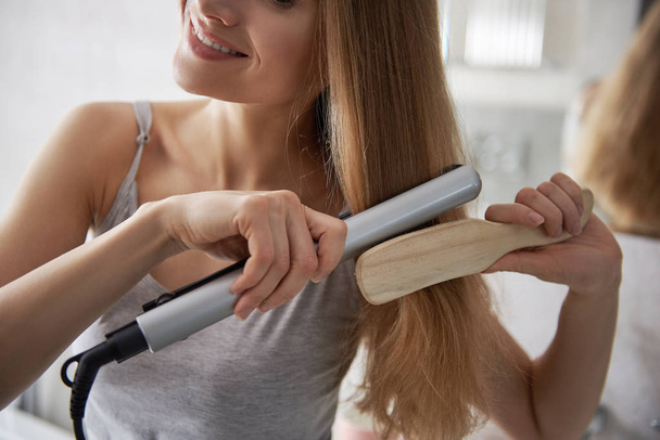 Pretty young lady using flat iron for hairstyle - Fotografie, Obrázek
