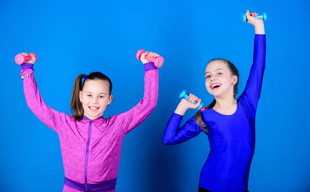 Easy exercises with dumbbell. Sporty upbringing. On way to stronger body. Girls exercising with dumbbells. Beginner dumbbells exercises. Children hold dumbbells blue background. Sport for teens - Zdjęcie, obraz