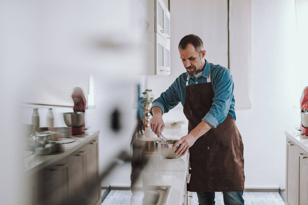 Concentrated bearded man whisking eggs on the countertop - Fotoğraf, Görsel