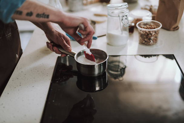 Man carefully putting spatula into the saucepan with milk - Фото, изображение