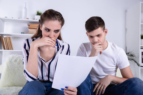 Happy couple reading mail and checking accountancy looking each other sitting on a couch at - Photo, Image