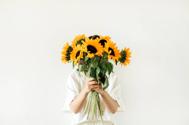 Young pretty woman in white dress hold sunflowers bouquet on white background. Florist minimal concept. - 写真・画像