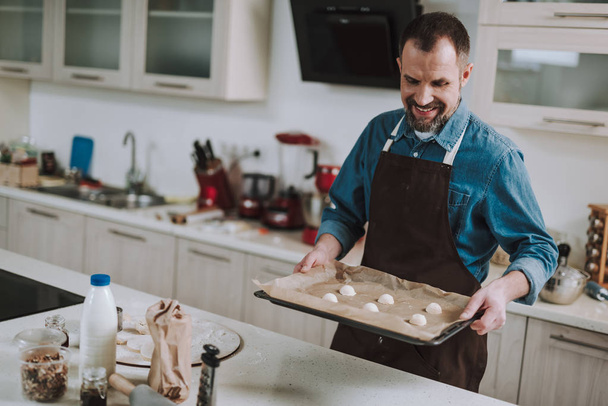 Cheerful man holding sheet pan with pastry and smiling - Foto, afbeelding