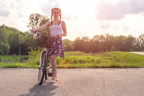 Ενεργός ζωή. Μια νεαρή γυναίκα με ποδηλασία στο ηλιοβασίλεμα στο πάρκο. Σχεδιασμός τρόπου ζωής ποδηλάτων και οικολογίας. - Φωτογραφία, εικόνα