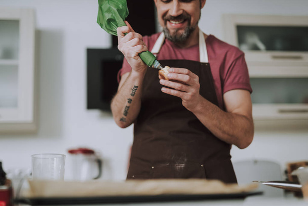 Positive bearded man smiling happily while using icing bag - Fotografie, Obrázek