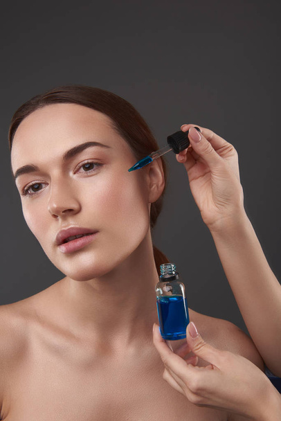 Beautician applying vitamin serum on lady face - Foto, imagen