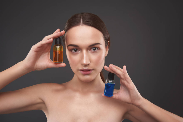 Charming young woman demonstrating vitamin serums for face - 写真・画像
