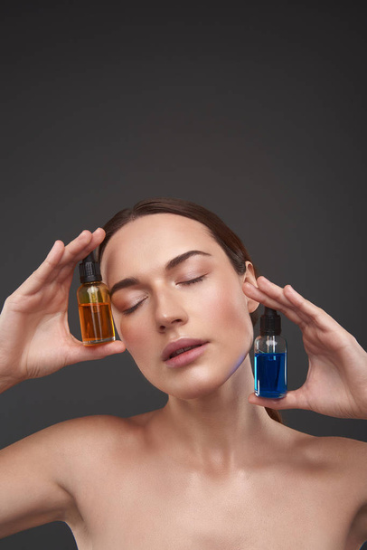 Serene pretty lady with closed eyes demonstrating vitamin serums for face - Zdjęcie, obraz