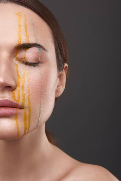 Serene young lady with orange and blue liquid dripping from her face - Photo, Image
