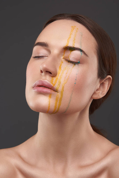 Serene attractive lady with orange and blue liquid dripping from her face - Foto, afbeelding