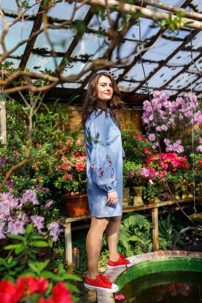 portrait of a young beautiful woman in a blue dress in a beautiful botanic garden with flowers - Photo, Image