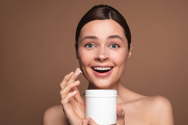 Excited woman using facial cream from the white jar - Photo, image