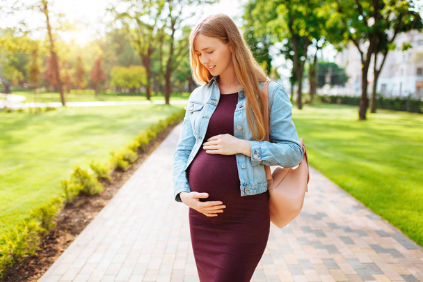 Happy pregnant girl is hugging her belly while walking in the pa - Foto, Bild