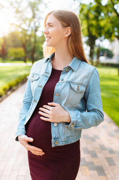 Happy pregnant girl is hugging her belly while walking in the pa - Photo, Image