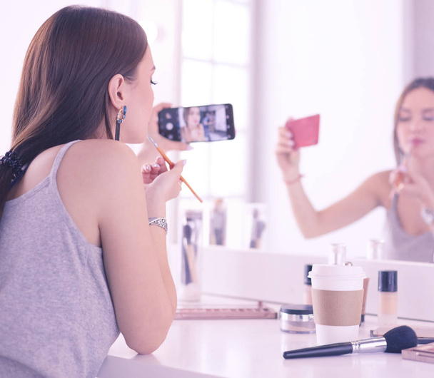 Blogger de belleza filmando tutorial de maquillaje con teléfono inteligente frente al espejo
 - Foto, imagen
