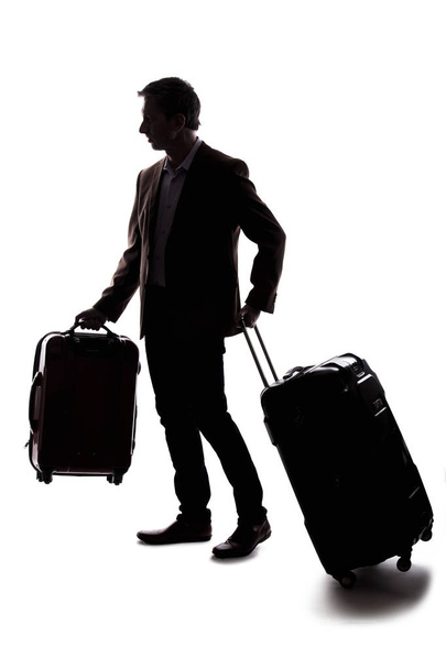 Silhouette of a businessman going on a business trip and traveling with luggage.  The man is carrying bags like preparing to board a flight at an airport.  - Valokuva, kuva