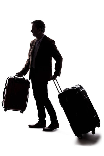 Silhouette of a businessman going on a business trip and traveling with luggage.  The man is carrying bags like preparing to board a flight at an airport.  - 写真・画像