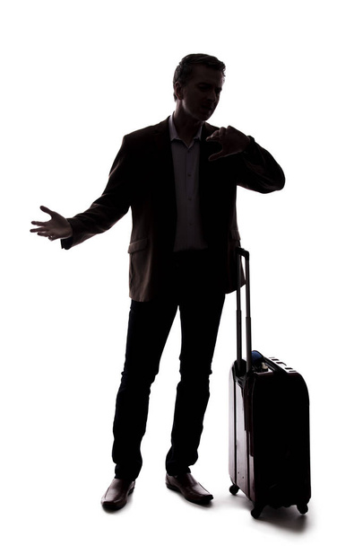 Silhouette of a traveling businessman looking upset because of a delayed or cancelled flight.  The traveler is stressed and waiting with his luggage.  Isolated on a white background. - Photo, Image