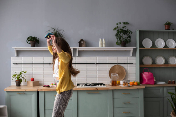 Stylish happy brunette girl in snake printed trousers dancing in the kitchen. - Photo, Image