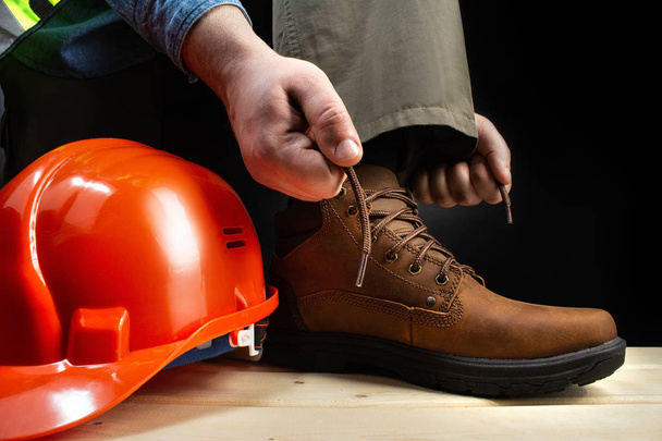 Worker with helmet lacing up leather boots. - Φωτογραφία, εικόνα