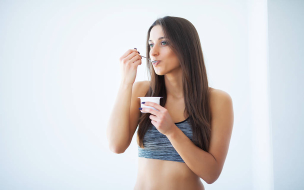 Diet. Happy young woman eating yogurt in kitchen - Photo, Image
