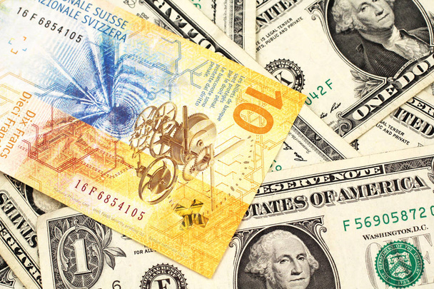 Ένα κίτρινο, δέκα ελβετικό φράγκο χαρτονόμισμα από την Ελβετία κλείνουν σε μακρο με αμερικάνικα χαρτονομίσματα του ενός δολαρίου - Φωτογραφία, εικόνα