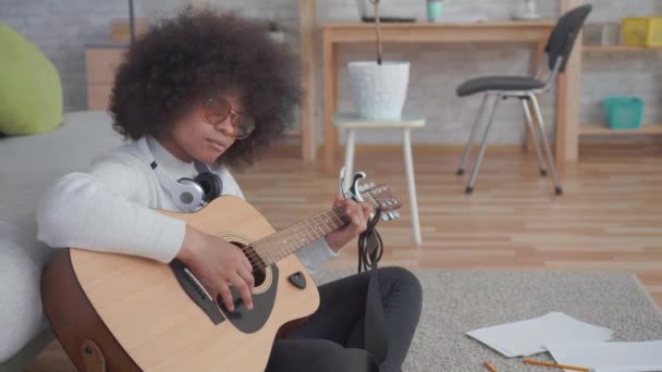 Portrait african american woman with an afro hairstyle plays guitar sitting on the floor - Footage, Video