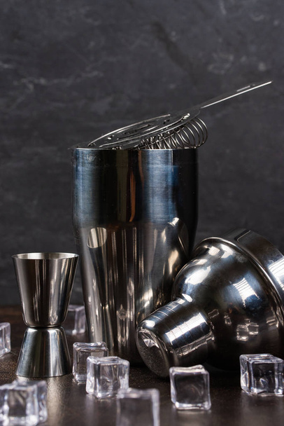 Stainless cocktail shaker and bar utensils with ice cubes on table, still life - Fotó, kép