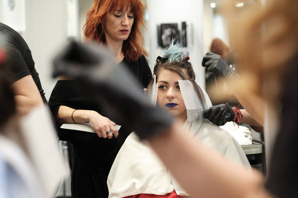dos peluquero joven teñir el pelo de cliente femenino mientras ella está sentada en la silla
 - Foto, Imagen