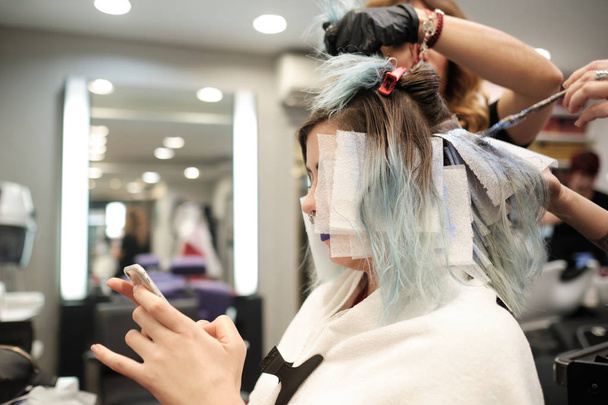 dos peluquero joven teñir el pelo de cliente femenino mientras lee su móvil
 - Foto, imagen