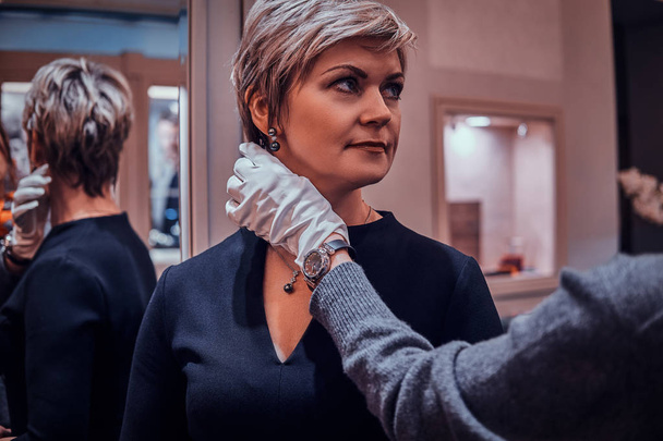 Κομψή γυναίκα προσπαθεί σε όμορφα σκουλαρίκια με βοηθούς κατάστημα βοήθεια σε πολυτελή κοσμήματα μπουτίκ - Φωτογραφία, εικόνα
