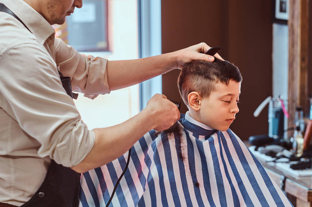 Mały chłopiec szkoły miał swój pierwszy modny fryzura w nowoczesnym Barbershop. - Zdjęcie, obraz