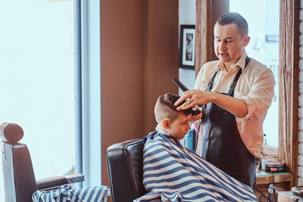 Pequeño colegial está consiguiendo corte de pelo de moda de peluquero expirienced en la barbería moderna
 - Foto, Imagen
