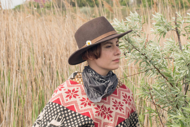 Genç kadın gezgin poncho ve şapka alanları ve çiftlikte yürümek - Fotoğraf, Görsel