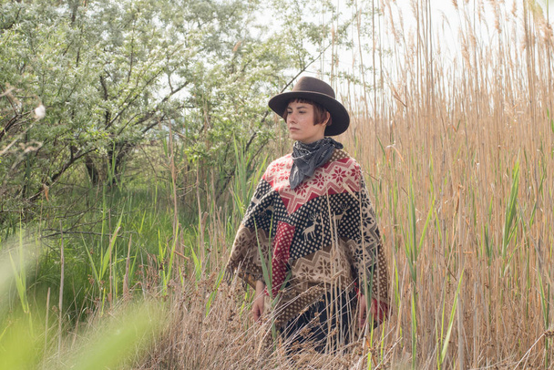 Jonge vrouw reiziger in poncho en hoed lopen in de velden en boerderij - Foto, afbeelding